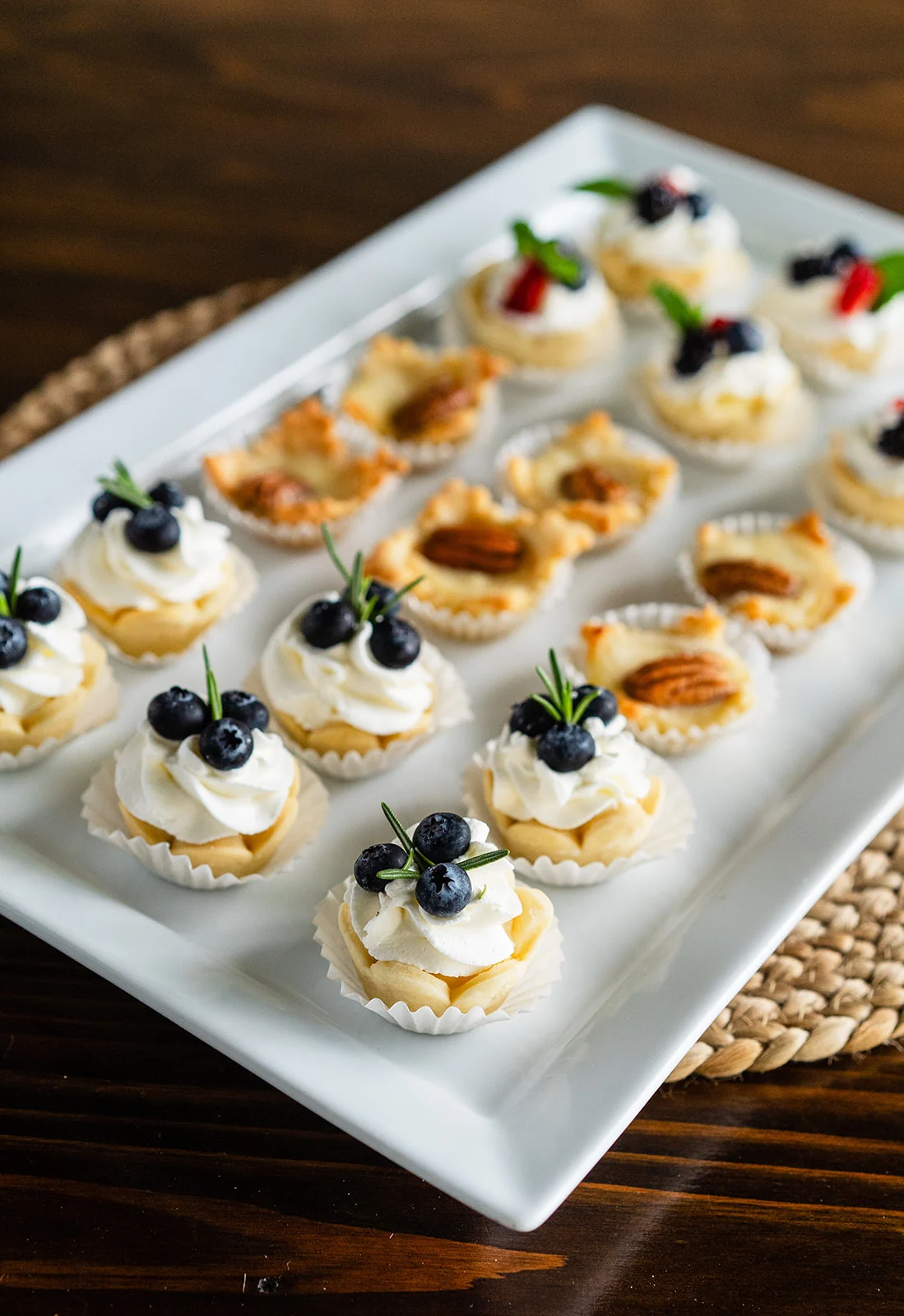 Mini tartlets topped with berries, whipped cream, and pecans on a white serving platter