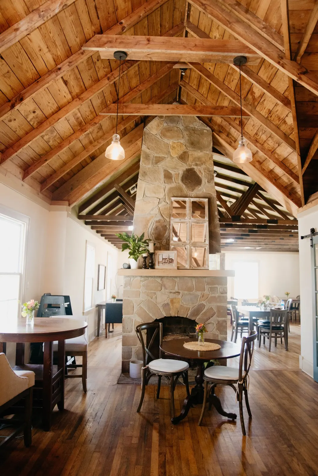 The bakery dining room with a stone fireplace, wood-truss ceiling, and tables on hardwood floors