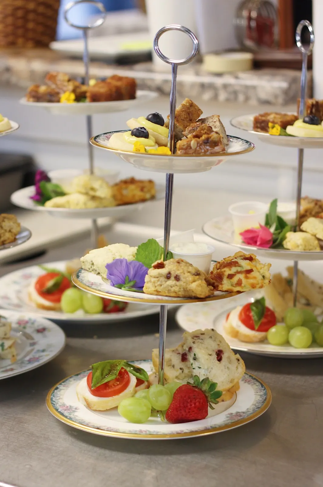 A three-tier tea stand with cookies, scones, fruit, and a caprese crostini